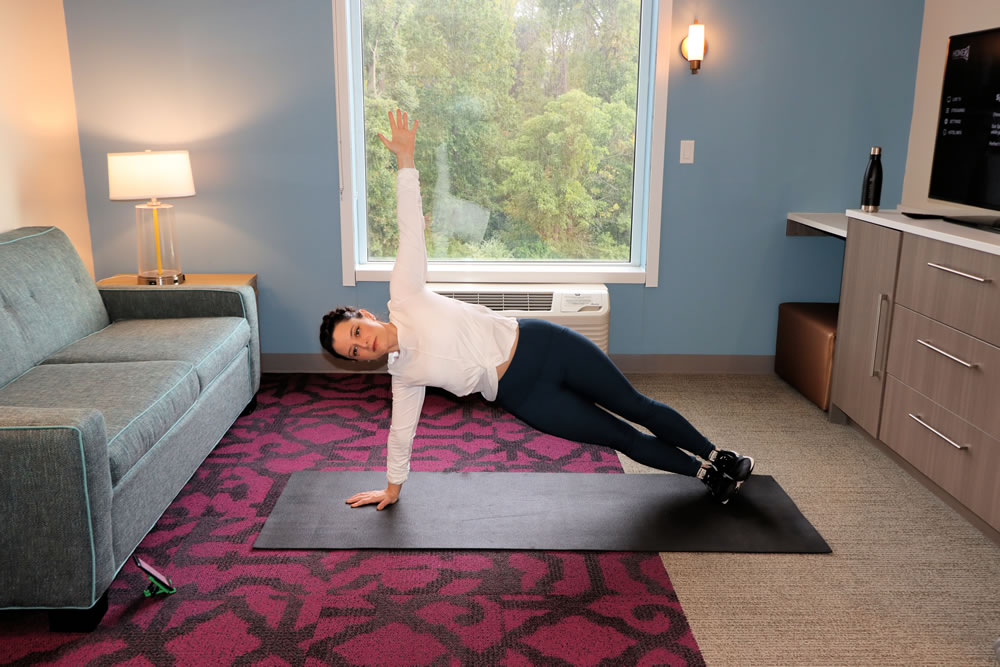 Fit woman doing bodyweight exercises outdoors on yoga mat with ocean view, demonstrating travel fitness routine