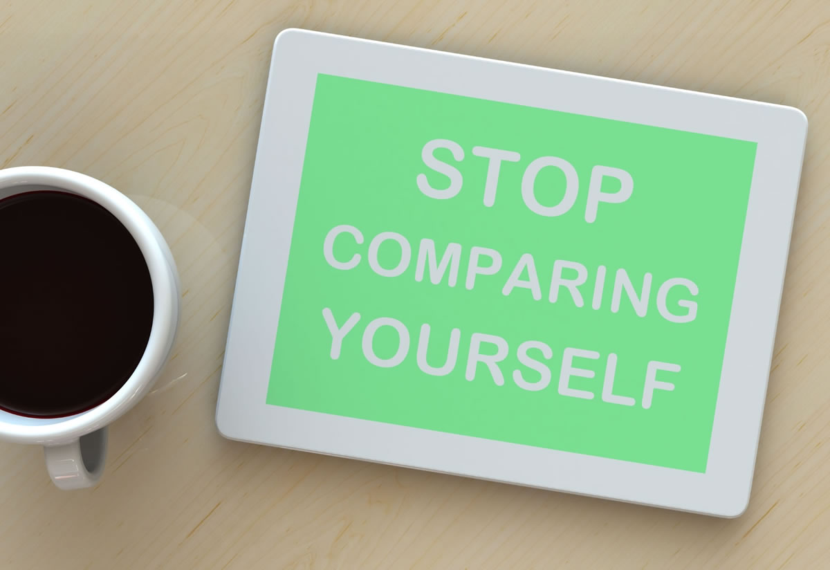 A sign reading 'stop comparing yourself' on a table next to coffee representing mindset for achieving fitness goals