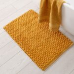 A bath mat on the floor next to a tub and towel, ready to be cleaned.