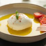 Close-up of burrata cheese with cherry tomatoes and olive oil in a sunny kitchen