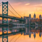 A romantic view of the Philadelphia skyline, water, and bridge at sunset.