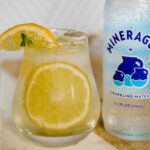 a bottle of sparkling water next a filled glass with lemon